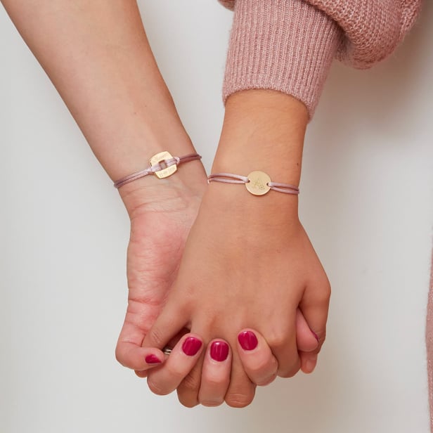 Photo du bracelet cordon personnalisé enfant lettre florale avec médaille plaqué or. Le bracelet est porté sur une jeune fille.