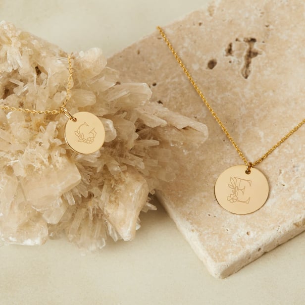 Nature morte collier personnalisé femme avec lettre florale sur médaille plaqué or
